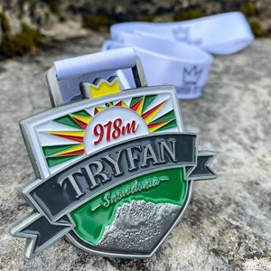 May include: A silver medal with a green, white, and red design. The medal features the text "Tryfan - Snowdonia" and "918m".