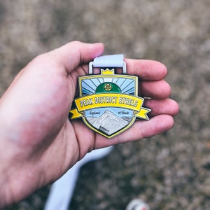 Op de afbeelding: Een zilveren medaille met een geel, groen en blauw ontwerp. De medaille heeft de tekst "Peak District Ethels" en "England 95 Peaks".