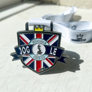 May include: A silver medal with a blue, white and red Union Jack design. The medal features the text "JOGLE" and "John O'Groats to Lands End" in white lettering. The medal is attached to a white ribbon with a crown logo.
