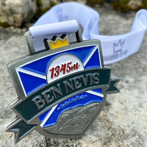 Op de afbeelding: Een zilveren medaille met een blauw en groen ontwerp. De medaille heeft een wit kruis met een rode cirkel waarop "1345m" staat en de tekst "BEN NEVIS" in een zwarte banner. De medaille is bevestigd aan een wit lint met een gouden kroon.