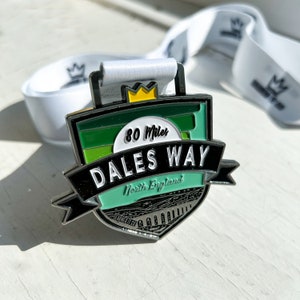 May include: A silver medal with a green, white and black design. The medal features the text "80 Miles Dales Way North England".