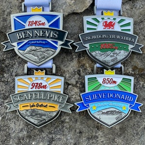以下が含まれることがあります： カラフルなデザインとテキストが施された銀製のメダル4つ。各メダルには山脈、王冠、山の名前が描かれています。メダルは、ベン・ネビス、スノードン、スカフェル・パイク、スリーヴ・ドナード用です。