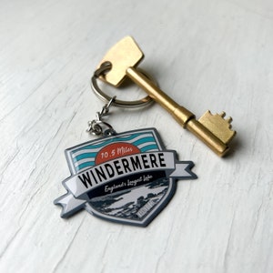 May include: A gold key charm with a blue and white enamel keychain featuring the text "10.5 Miles Windermere England's longest lake".