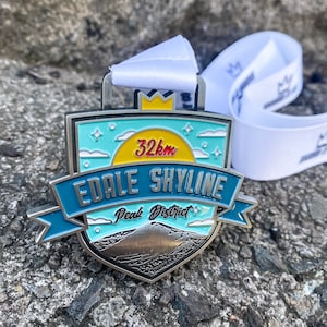 May include: A silver medal with a blue, yellow and white design. It says "32km Edale Skyline Peak District" on it.