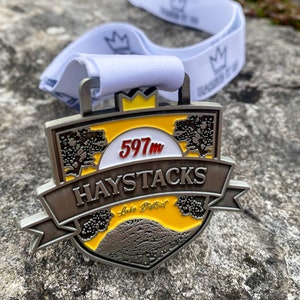 May include: A silver medal with a yellow and white design. The medal features the text "Haystacks" and "Lake District" and the number "597m".