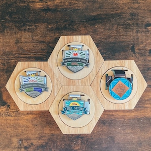 May include: Four wooden medal display stands with circular medal holders. The medals are silver and feature colorful designs with text. The text on the medals reads "Snowdon Yr Wyddfa", "Yorkshire Three Peaks", "Edale Skyline", and "10K Great Dodder", respectively.