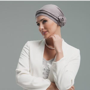 May include: A light grey head wrap featuring a twisted band design and a decorative fabric flower detail on the side. The head covering is made of a soft, smooth fabric and fits snugly around the head, providing full coverage in a neutral tone.