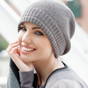 May include: A gray slouchy beanie hat with a ribbed texture. The hat is made of soft knit fabric and has a relaxed fit.