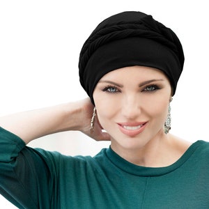 Puede incluir: Una mujer con un turbante negro y una camisa verde azulada. Está sonriendo y mirando a la cámara.