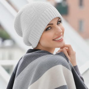 May include: A light gray knit beanie with a textured, waffle-like stitch pattern and a wide, ribbed cuff. The beanie is paired with a multi-toned scarf featuring diagonal stripes in shades of dark gray, light gray, and off-white.