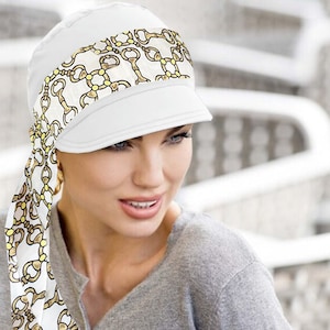 Könnte beinhalten: Eine weiße Baumwollkappe mit einem goldenen und gelben Kettenmuster. Die Kappe hat ein Visier und eine lange Krawatte, die am Hinterkopf gebunden ist.