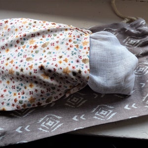 Peut inclure: Un sac à cordon brun avec un motif géométrique blanc. Le sac est ouvert et un sac en tissu blanc avec un motif floral est à l'intérieur.