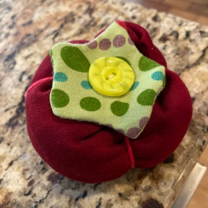 May include: A red fabric star with a green and purple polka dot fabric star on top. The top star has a yellow button in the center.