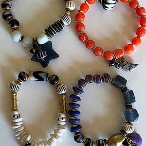 May include: Four beaded bracelets in various styles. One bracelet features black and white beads with a star charm. Another has red beads with a charm. The third has white and gold beads with a turquoise charm. The last has blue and black beads.