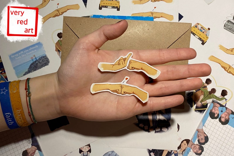 Op de afbeelding: Twee gele handgetekende stickers van twee mensen die een pinky promise doen. De stickers zitten op een hand met een blauwe en gele armband.