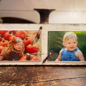 May include: A distressed white wooden double picture frame with two photos. One photo shows a child in a pumpkin costume, the other shows a baby in denim overalls. The frame has metal accents.