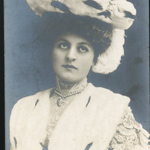 May include: A black and white portrait of a woman wearing a large white feathered hat and a white fur coat. The text "Miss Adele Ritchie" is printed below the image.