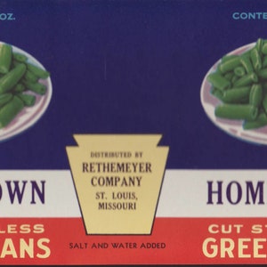 Op de afbeelding: Een blauw en rood etiket voor een blik Home Town Cut Stringless Green Beans. Het etiket toont een afbeelding van groene bonen op een bord en de tekst "CONTENTS 1 LB. 3 OZ.".