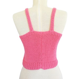 May include: A pink knitted tank top with thin straps. The tank top is sleeveless and has a cropped length.