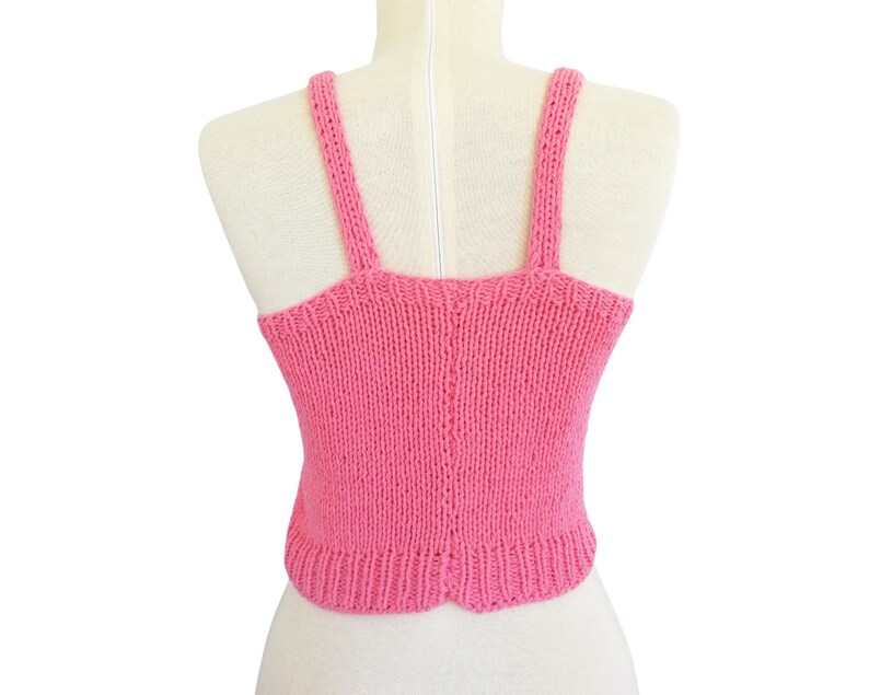 May include: A pink knitted tank top with thin straps. The tank top is sleeveless and has a cropped length.