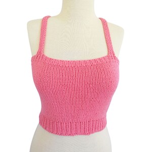 May include: A pink knitted crop top with thin straps. The top is made of a soft, lightweight yarn and has a relaxed fit.