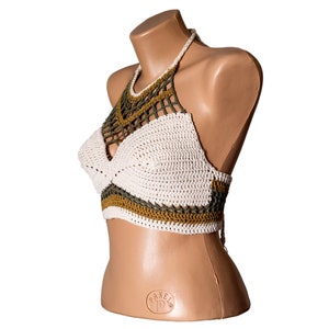 May include: White crochet halter top with green and brown accents. The top is made of a delicate crocheted fabric and has a halter neck style.