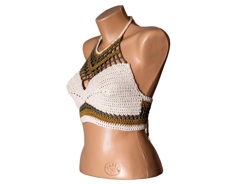 May include: White crochet halter top with green and brown accents. The top is made of a delicate crocheted fabric and has a halter neck style.