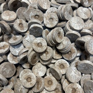 May include: A close-up shot of a pile of round, compressed soil discs. The discs are a light brown color with a textured surface and a central indentation. They are likely used for starting seeds or as a growing medium.