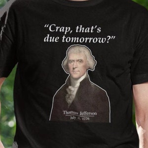 May include: Black t-shirt with a white graphic of Thomas Jefferson and the quote "Crap, that's due tomorrow?"  July 4, 1776.