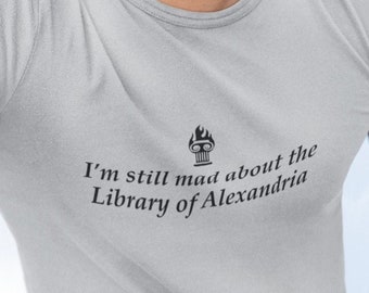 May include: A gray t-shirt with a black graphic of a burning torch and the text "I'm still mad about the Library of Alexandria".