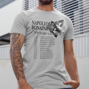 May include: A gray t-shirt with a black print of Napoleon Bonaparte's portrait and a list of his military victories from 1796 to 1815. The text reads "Napoleon Bonaparte Victory Lap Tour".