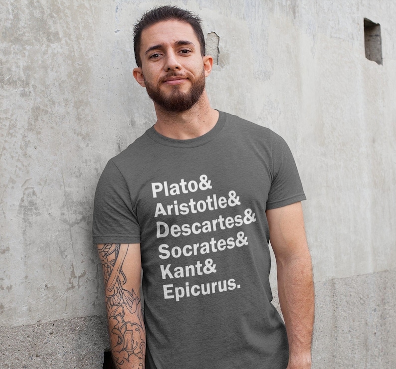 Puede incluir: Una camiseta gris oscura con texto blanco que dice "Plato & Arist&oacute;teles & Descartes & S&oacute;crates & Kant & Epicuro."