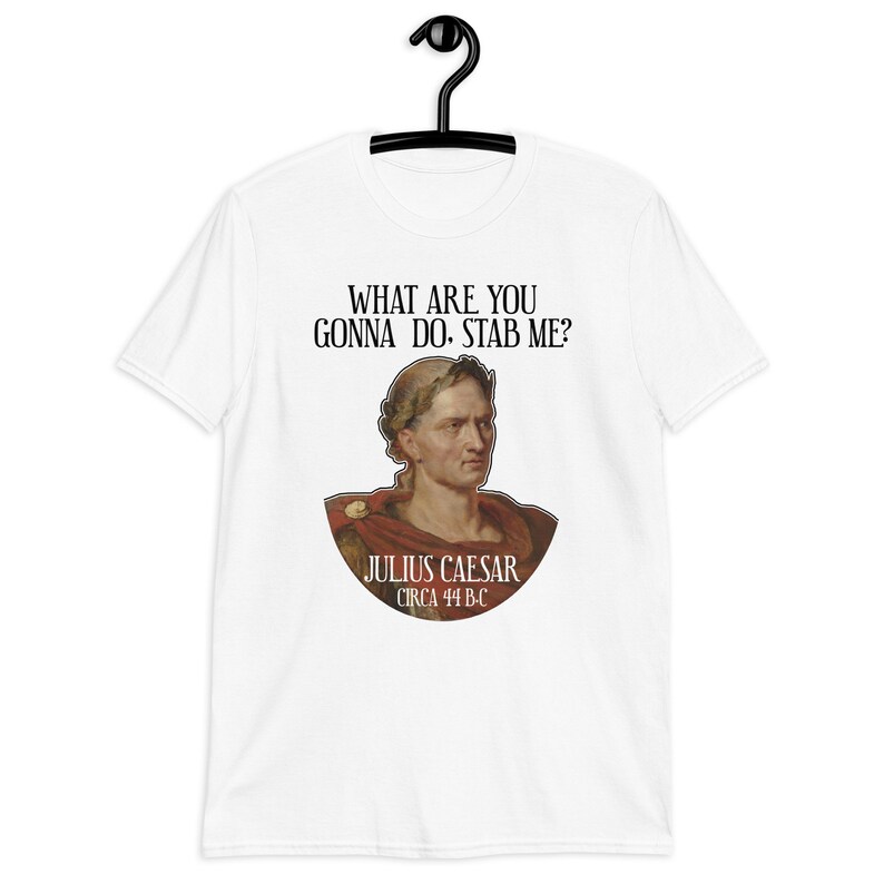 May include: White t-shirt with a graphic of Julius Caesar, a Roman general, with the text "WHAT ARE YOU GONNA DO. STAB ME?" and "JULIUS CAESAR CIRCA 44 B.C."