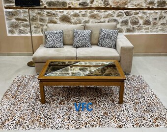 Puede incluir: Un sofá beige con tres cojines grises se encuentra frente a una pared de piedra. Una mesa de café de madera con tapa de vidrio se encuentra sobre una alfombra de estampado de leopardo frente al sofá.