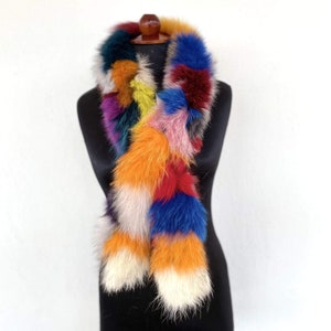 May include: A colourful fox fur scarf with a patchwork design. The scarf is made of different coloured fox fur pieces sewn together. The scarf is on a black mannequin.