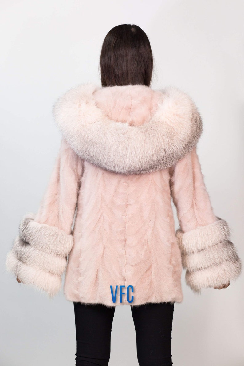 Puede incluir: Un abrigo de piel rosa con un gran cuello y pu&ntilde;os de piel blanca. El abrigo tiene un logotipo VFC en la espalda.