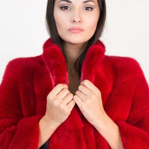 Peut inclure: Une femme portant un manteau en fourrure rouge avec un logo VFC en bas. Elle tient le col du manteau ferm&eacute;.