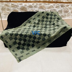 Pode incluir: Uma manta de l&atilde; xadrez verde e preta com as letras "VFC" em azul na manta.