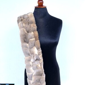 May include: A long, light brown fur scarf with a braided design. The scarf is draped over a black mannequin.