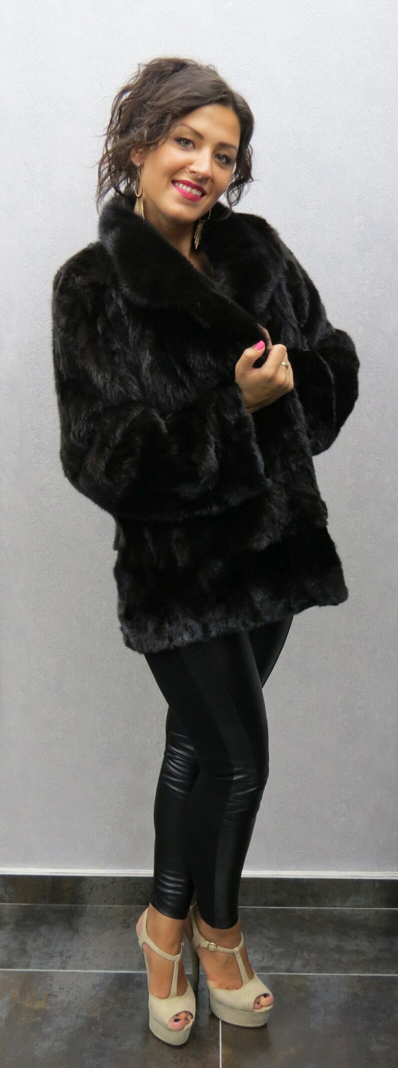 Puede incluir: Una mujer con un abrigo de piel negro con un cuello grande, leggings negros y tacones de plataforma beige.