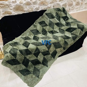Puede incluir: Una manta de tiro con estampado geom&eacute;trico verde y negro con un logotipo VFC en el centro.