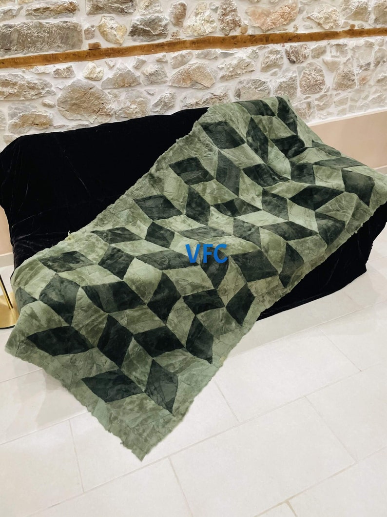 Puede incluir: Una manta de tiro con estampado geom&eacute;trico verde y negro con un logotipo VFC en el centro.