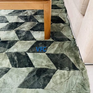 Puede incluir: Una alfombra de patr&oacute;n geom&eacute;trico verde y negro con una mesa de caf&eacute; de madera en la parte superior. La alfombra tiene una textura peluda.