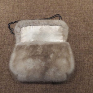 May include: A light grey fur handbag with a chain strap. The bag is open and the inside lining is white.