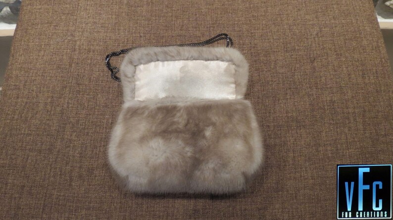 May include: A light grey fur handbag with a chain strap. The bag is open and the inside lining is white.