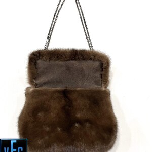 May include: A brown fur handbag with a silver chain strap. The bag is open and the inside lining is visible.
