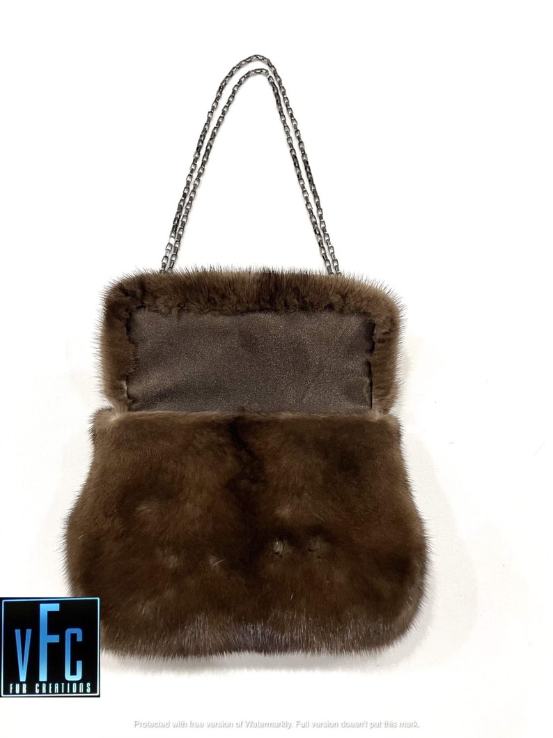 May include: A brown fur handbag with a silver chain strap. The bag is open and the inside lining is visible.