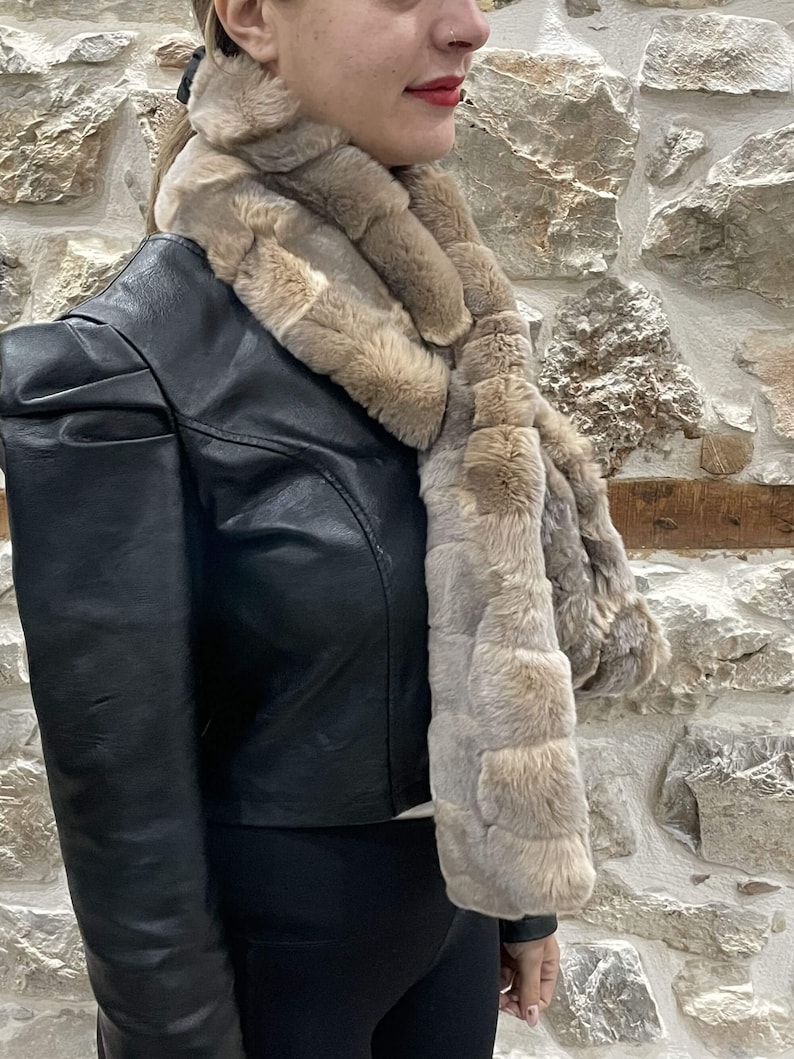 May include: A brown faux fur scarf with a long, rectangular shape. The scarf is made of soft, fluffy fur and has a subtle pattern. It is worn by a person wearing a black leather jacket.