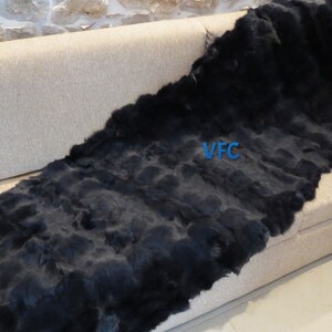 May include: A black rabbit fur throw blanket is draped over a light brown couch. The blanket is made of many strips of fur sewn together. The text "VFC" is visible on the blanket.