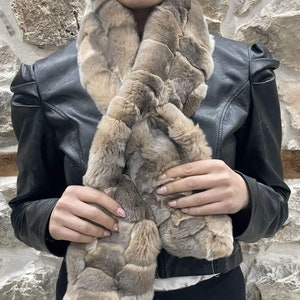 May include: A brown faux fur scarf with a textured pattern. The scarf is worn around the neck of a person wearing a black leather jacket.
